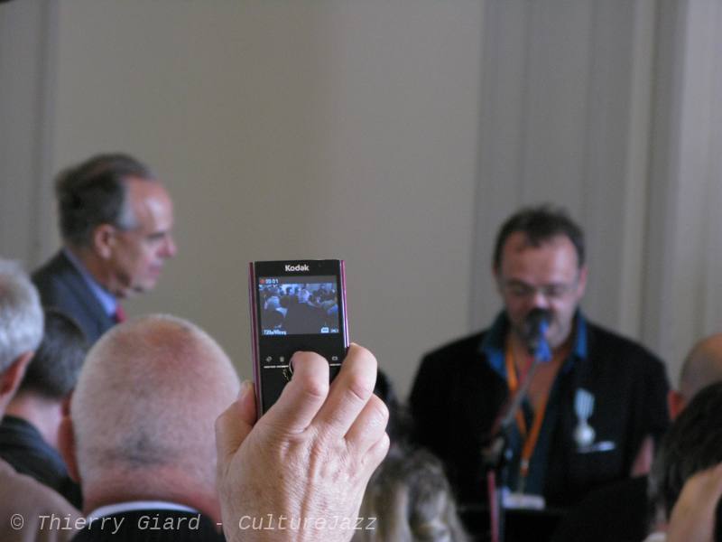 DenisLeBas-F-Mitterrand_04juin2011_w.jpg - Le ministre de la Culture, Frédéric Mitterrand était à Coutances pour la conclusion du festival et pour remettre à Denis Le Bas la médaille de Chevalier des Arts et des Lettres. Une marque de reconnaissance pour tout le travail effectué par Denis Le Bas et son équipe de professionnels (et de bénévoles) pour faire vivre la culture dans cette petite ville de 10 000 habitants. Armé de son camescope "compact", c'est le tromboniste Glenn Ferris qui immortalise cet instant ! (T.G.)